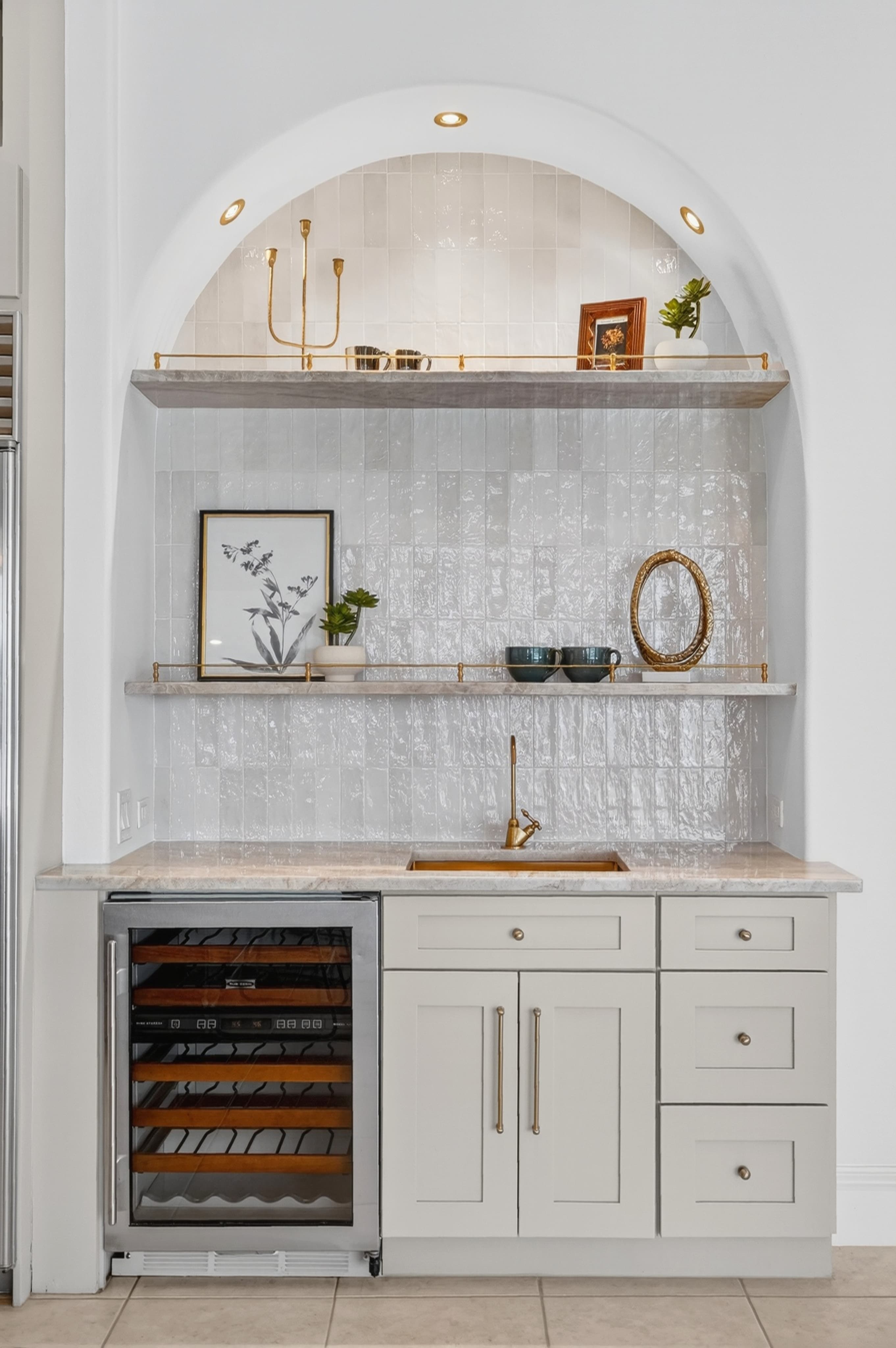 Arched wet-bar nook with white tile, brass faucet, and integrated wine fridge