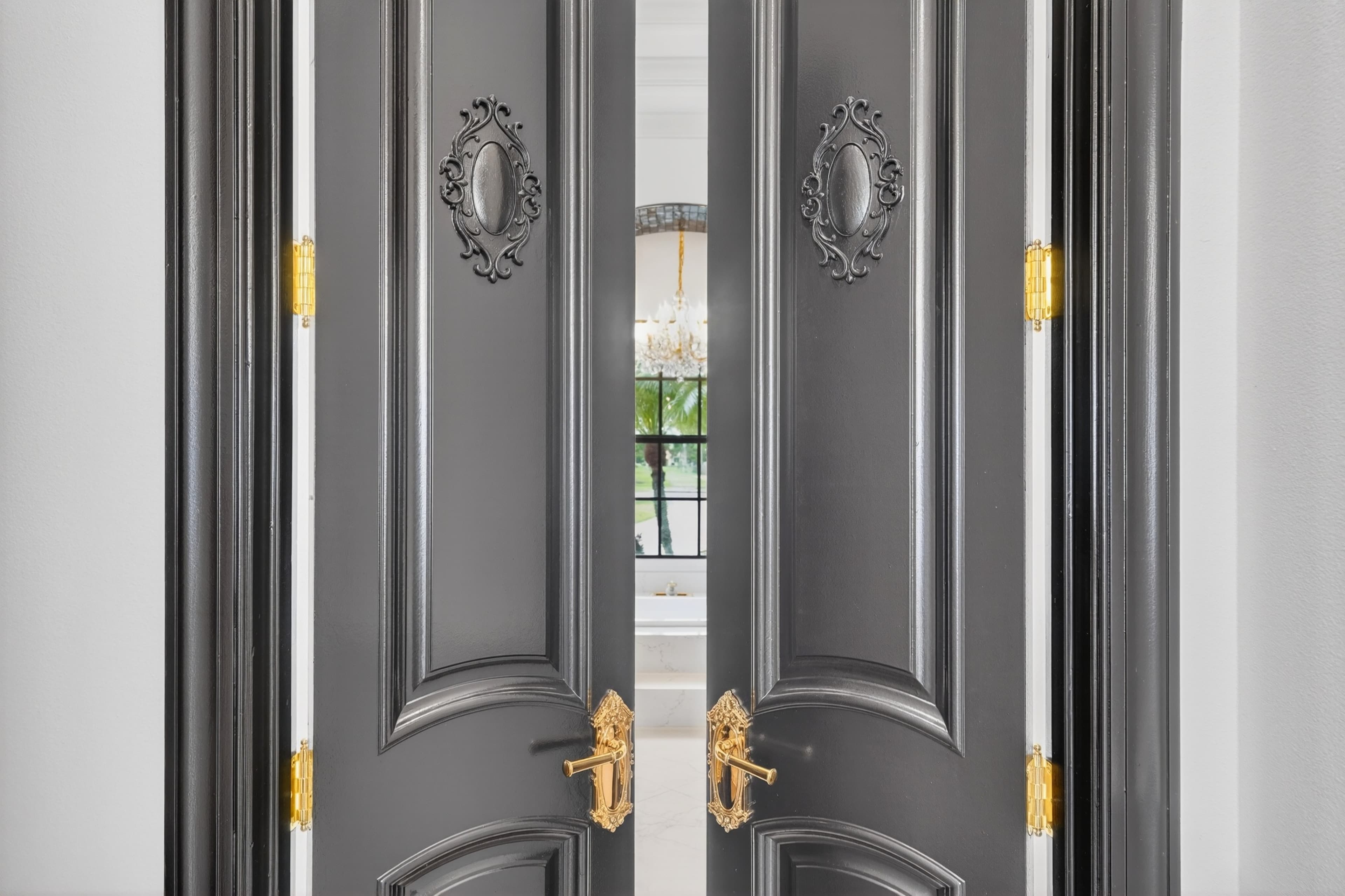 Ornate double doors opening onto a chandelier-lit primary bath beyond