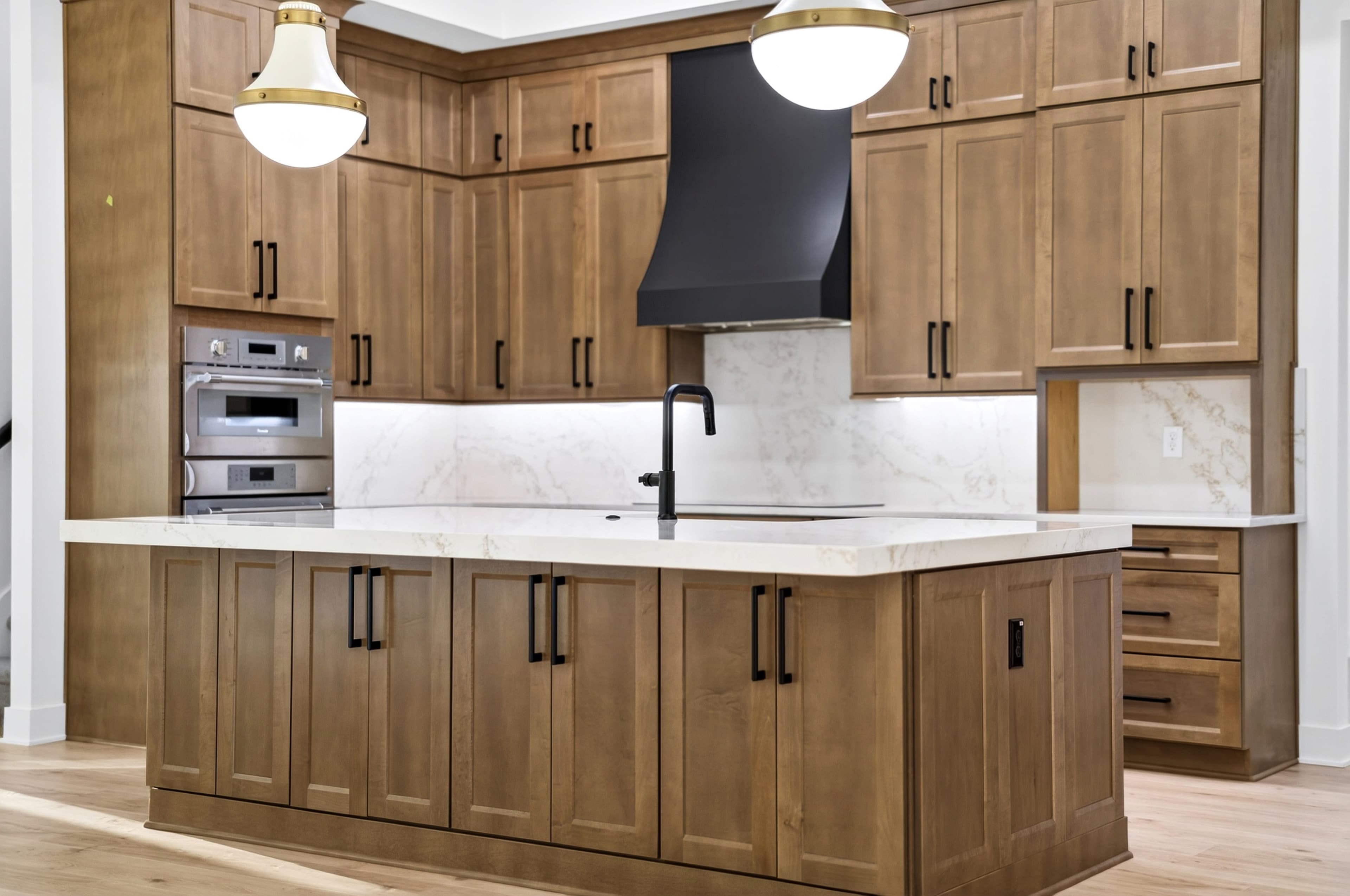 Wood-cabinet kitchen with marble counters, brass pendants, and matte-black hood