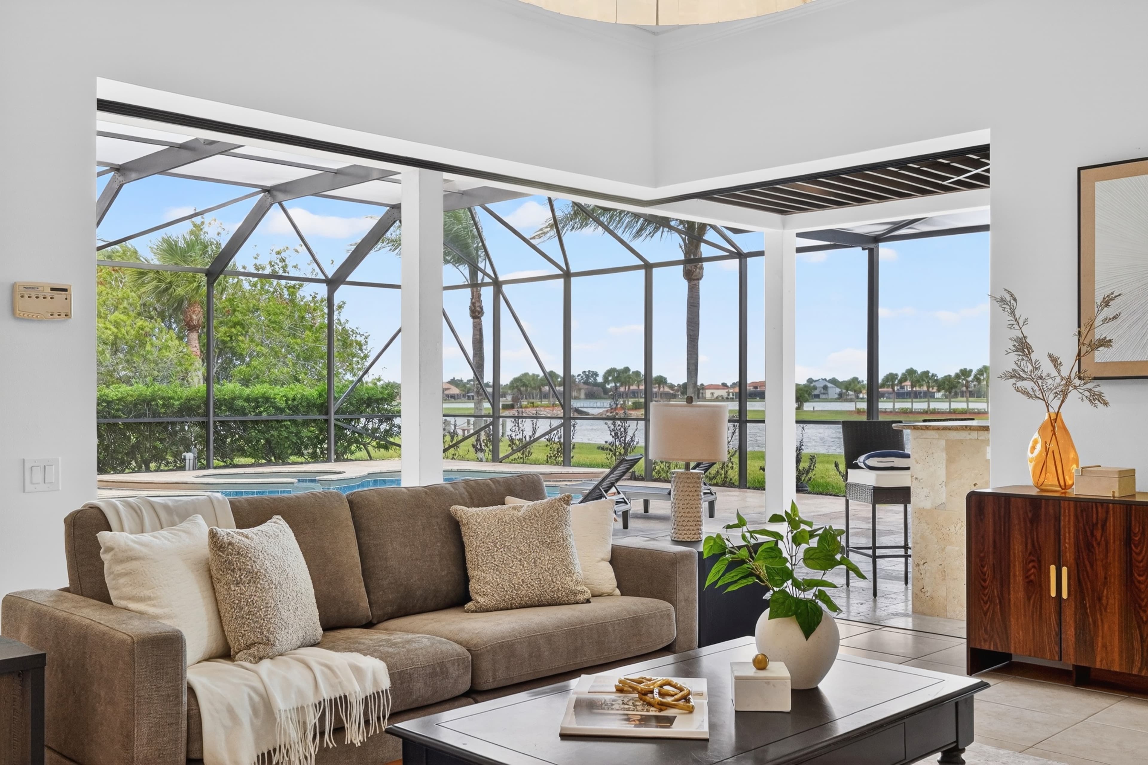 Staged living room opening to a screened lanai with pool and lake beyond