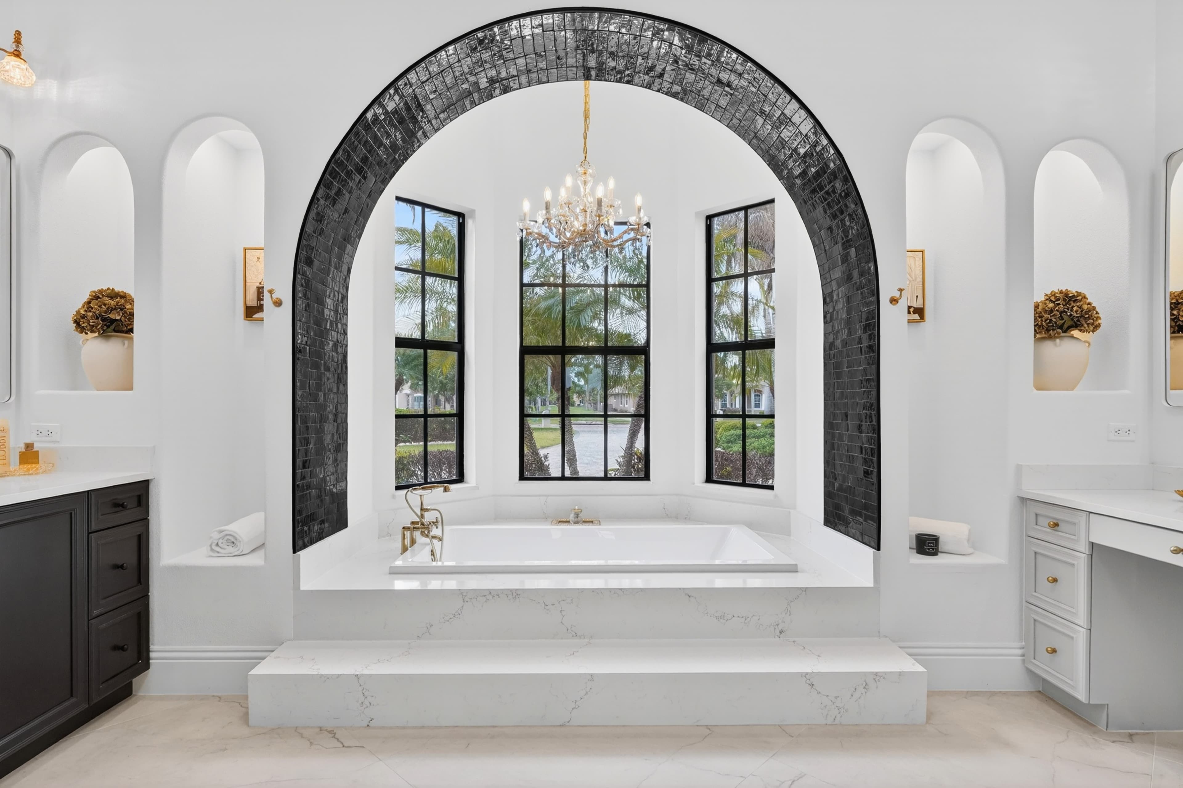 Primary bath with arched tile niche, freestanding tub, and crystal chandelier